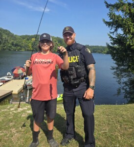 A boy holding a fishing rod and fish stands beside a police officer