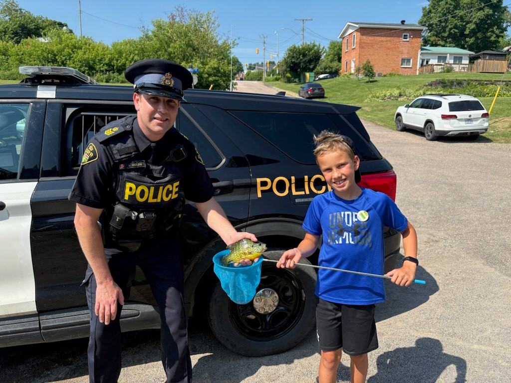 a police officer poses with a child holding a fish they caught