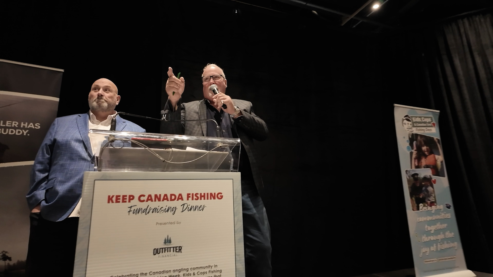 two men stand at a podium that says, Keep Canada Fishing Fundraising Dinner