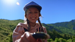 A young girl holds a trout while smiling