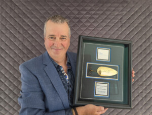 Patrick Campeau stands holding a plaque and award.