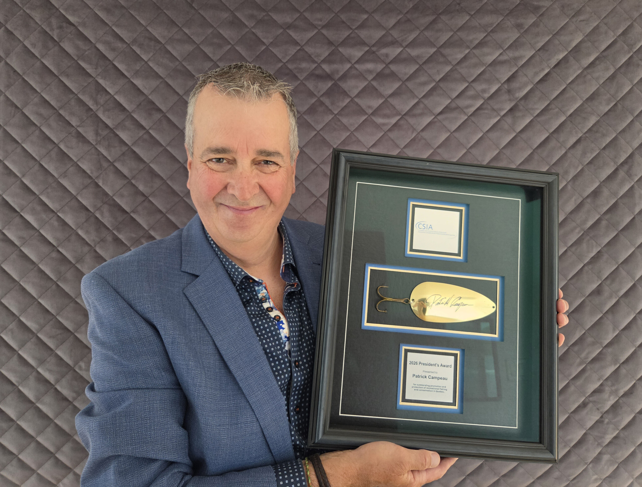 Patrick Campeau stands holding a plaque and award.